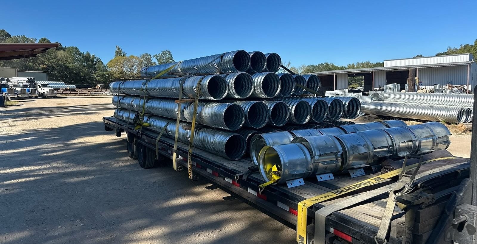 Bundles of galvanized culvert pipe stacked and strapped across a flatbed trailer